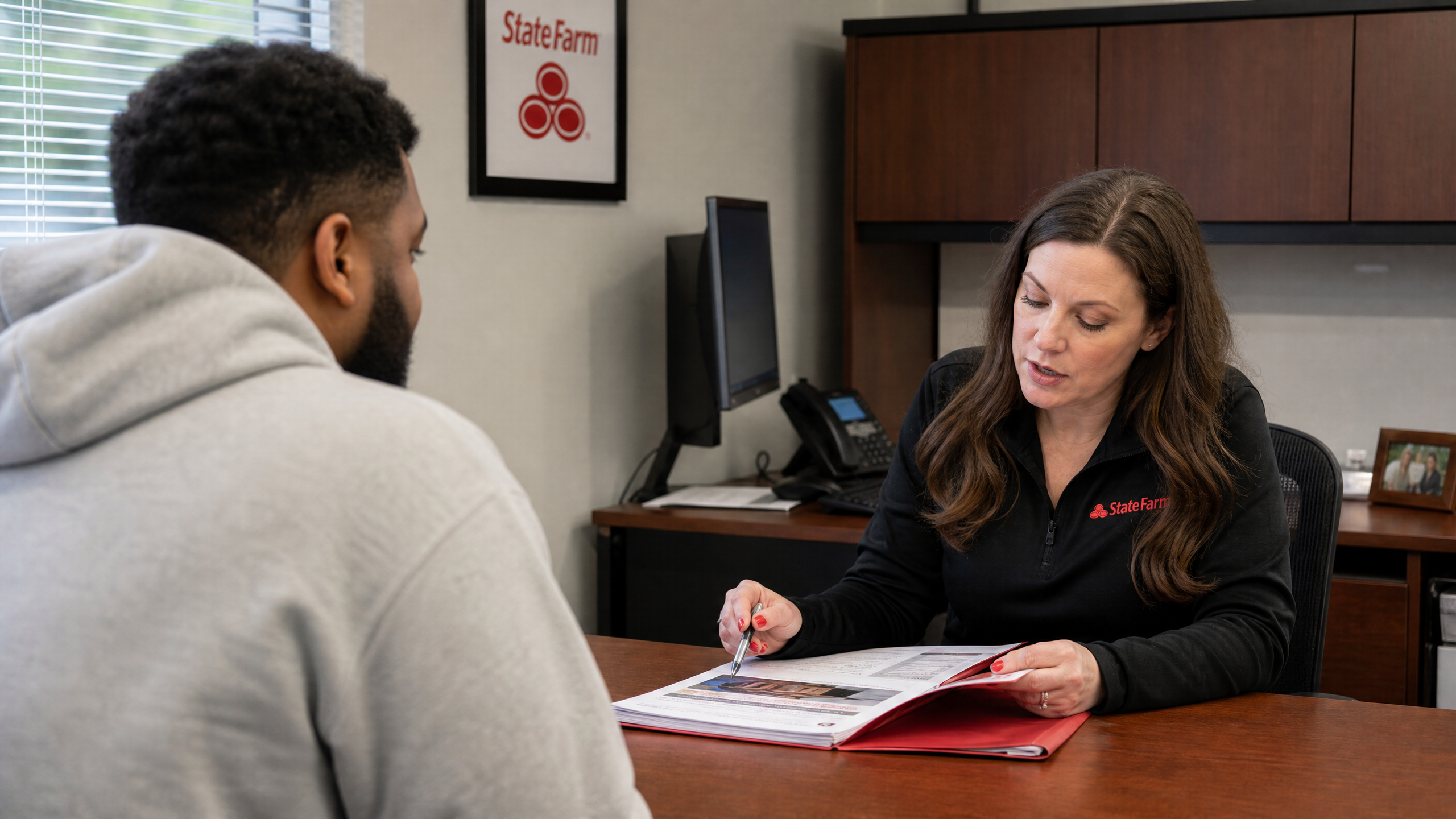 Insurance agent reviewing a State Farm total loss claim folder with a customer across a desk, explaining how actual cash value is determined